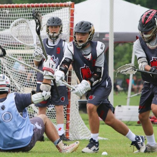 A lacrosse player defends the goal against an attack from an opposing player.