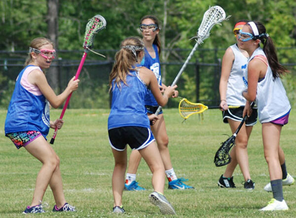 Youth lacrosse players practicing on a field, wearing blue and white jerseys, holding lacrosse sticks.